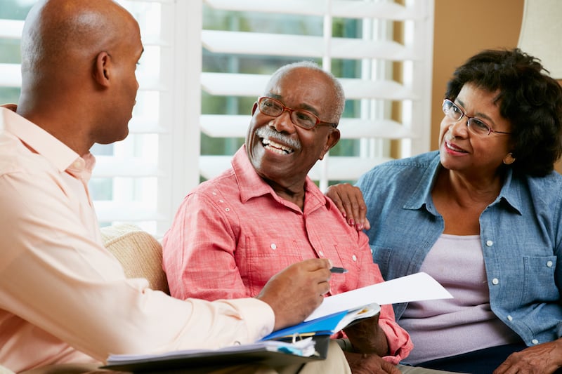 An older adult smiles warmly while seated between two younger companions who review paperwork together, reflecting supportive family conversations about assisted living in Fort Myers, FL.