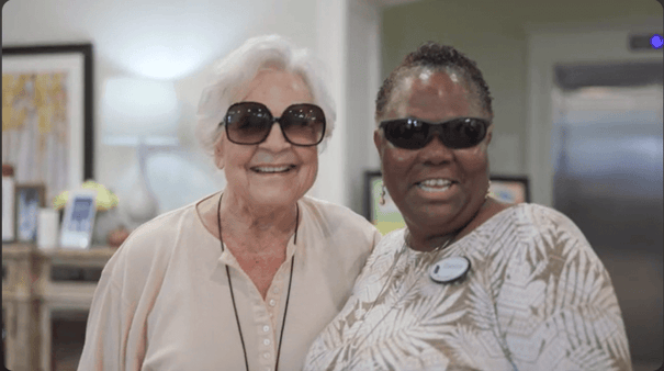 Two women wearing sunglasses smile together indoors, sharing a joyful moment that reflects the warm community spirit at senior living in Suwanee, GA.