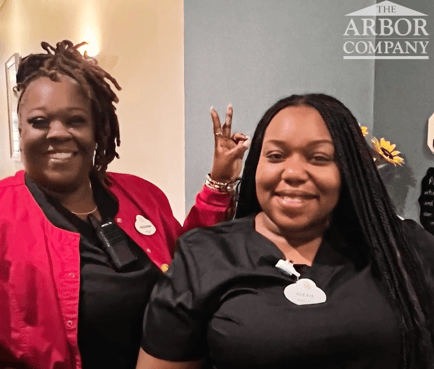 Two Arbor Terrace Athens team members wearing name badges smile and pose playfully together, showcasing the warm, spirited culture at this senior living community in Athens, GA.