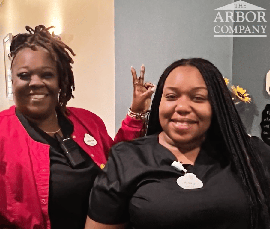 Two Arbor Terrace Athens team members wearing name badges smile and pose playfully together, showcasing the warm, spirited culture at this senior living community in Athens, GA.