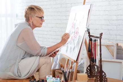 A resident focuses intently on painting a floral canvas at an easel, showcasing the creative and engaging senior living activities offered at our community in Gambrills, MD.