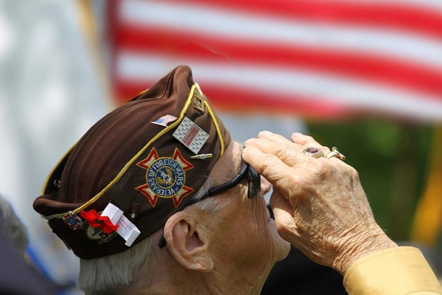 A veteran in a military cap offers a salute beside an American flag at this senior living community near Greenbelt, MD, which proudly honors and celebrates its veterans through meaningful community events.