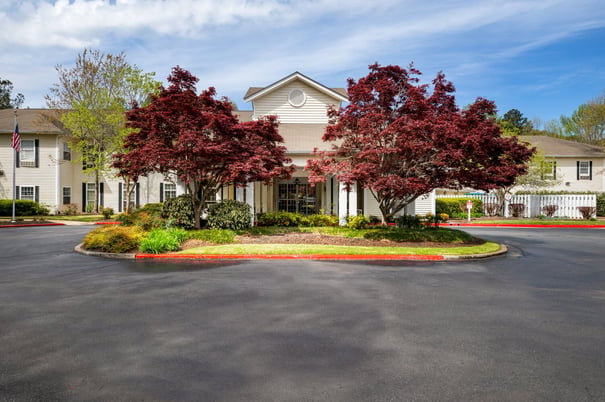 The welcoming exterior of Arbor Terrace Athens, a senior living community in Athens, GA, featuring vibrant red Japanese maple trees, manicured landscaping, and a circular drive on a bright, sunny day.