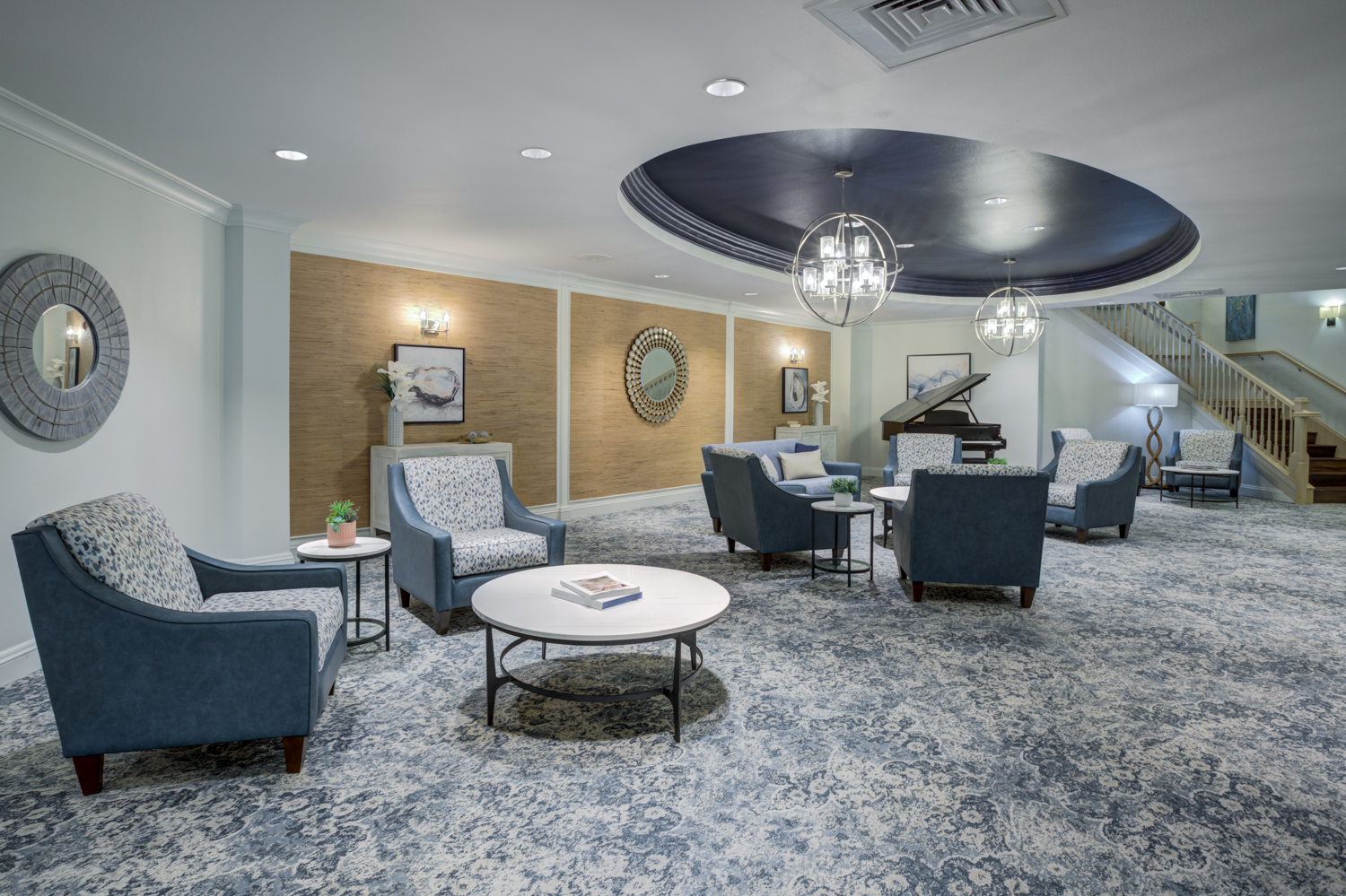 A beautifully appointed common area with plush seating, a coffered ceiling, and a grand piano, showcasing the resort-style senior living in Citrus Park, FL.