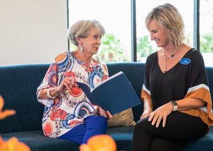 two senior ladies sitting down on a sofa and sharing a book