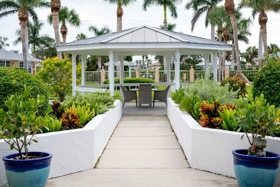 The welcoming entrance of Barrington Terrace of Fort Myers features warm peach-toned walls, lantern sconces, lush potted plants, and open glass doors revealing a cozy interior seating area.