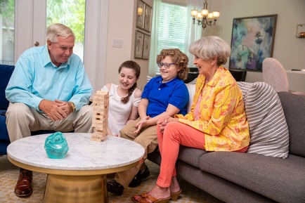 Two older adults enjoy a cheerful game of Jenga with two children in a cozy living room, reflecting the warm, family-centered community life at Arbor Terrace Morris Plains, NJ.