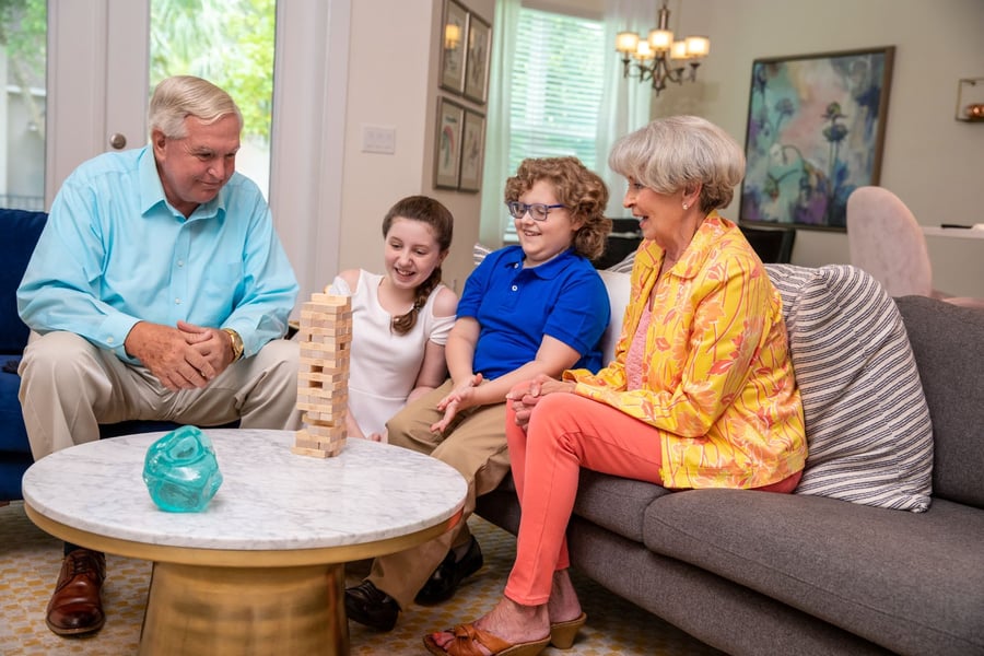 Two older adults enjoy a cheerful game of Jenga with two children in a cozy living room, reflecting the warm, family-centered community life at Arbor Terrace Morris Plains, NJ.