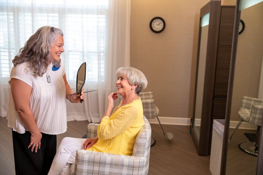 A staff member helps a resident get ready with a hand mirror in a well-appointed bedroom, reflecting the wellness-focused care found at Glenview senior living.