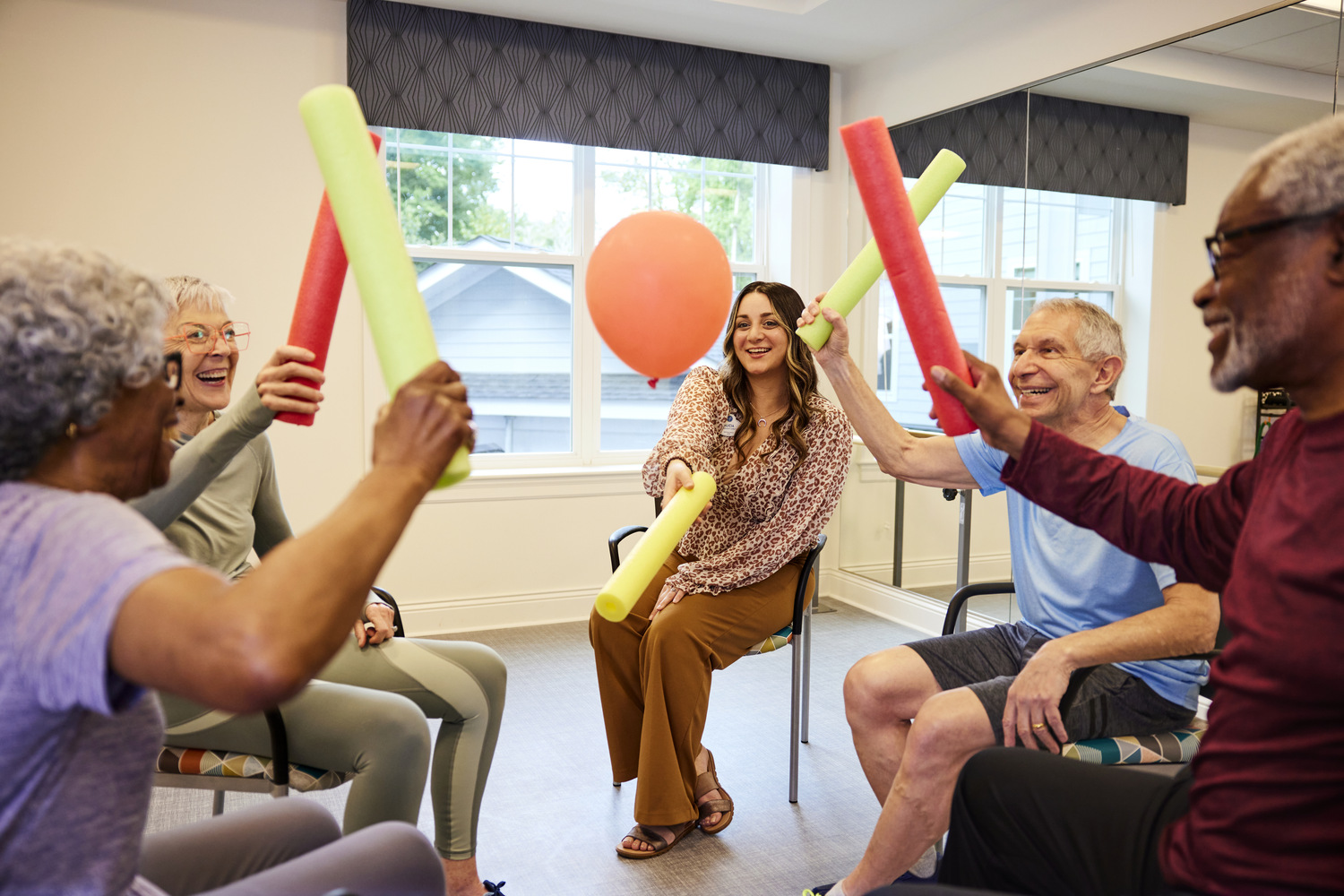 Residents enjoy an energetic group activity with pool noodles and balloons, reflecting the active senior lifestyle and wellness programs at Glenview senior living.