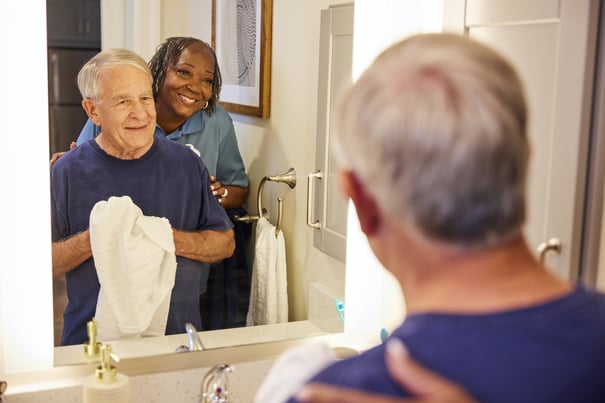 A smiling staff member assists an older adult at a bathroom mirror — compassionate, hands-on senior care Lakeway TX when evaluating assisted living community Lakeway staff.