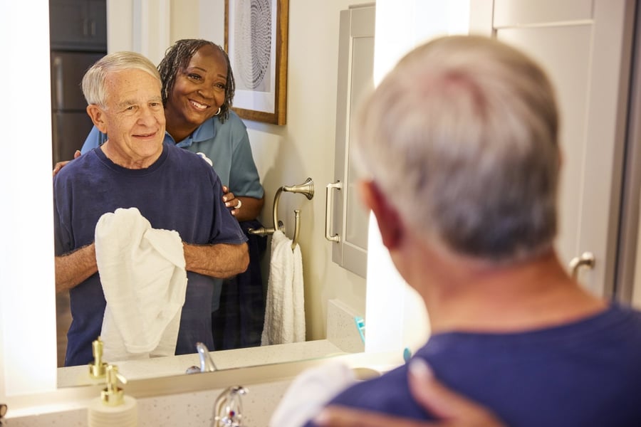 a senior man being assisted by a staff by the bathroom sink