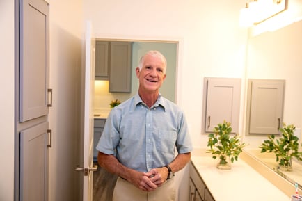 An older adult smiles warmly while standing in a bright, well-appointed bathroom, reflecting the comfortable and thoughtfully designed assisted living apartments at Arbor Terrace Morris Plains, NJ.