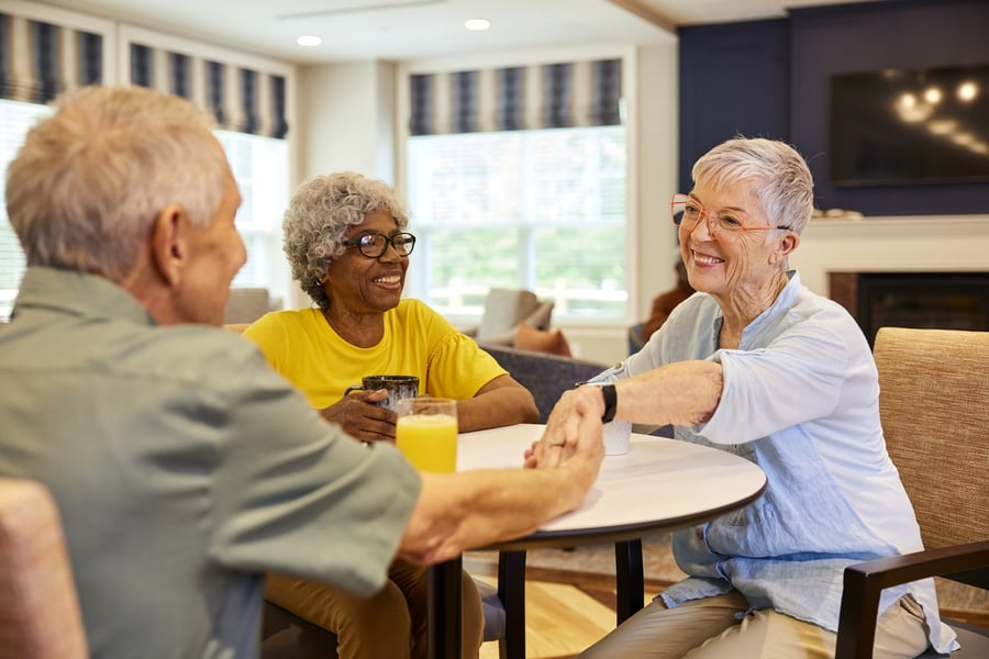 Three seniors sit around a table chatting and holding drinks in a bright, welcoming common area — early cognitive support Lakeway through the Connections Program for early memory loss.
