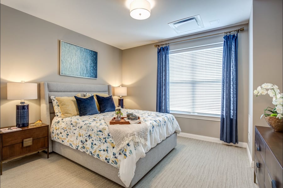 A cozy, well-appointed bedroom featuring soft linens and warm lighting showcases the resort-style senior living apartments available in Glenview, IL.