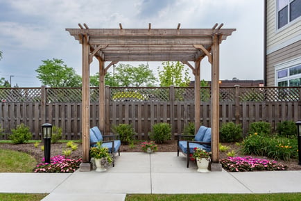 A shaded pergola with cozy seating surrounded by blooming flowers highlights the outdoor amenities of Glenview senior living on the North Shore.