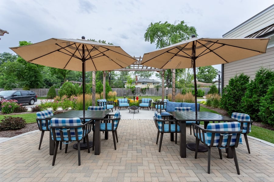 A shaded outdoor patio with plaid cushioned seating showcases the inviting outdoor amenities at an assisted living community in Glenview, Illinois.