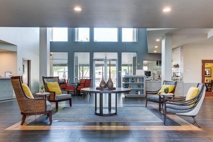 A spacious, light-filled common area at Arbor Terrace Lakeway featuring high ceilings, large windows, and comfortable seating with yellow accent pillows — welcoming senior living Lakeway Texas.