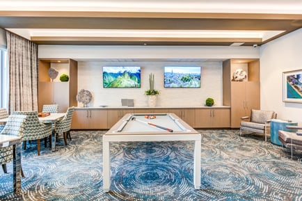 A stylish game room at Mirabelle features a pool table, flat-screen TVs, and elegant decor, offering residents a fun and sophisticated space to enjoy independent living in Miami, FL.