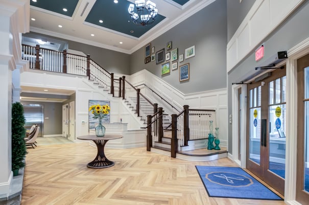 The grand, light-filled entryway at Arbor Terrace Morris Plains features elegant hardwood floors, a sweeping staircase, and fresh floral accents, welcoming residents and families to this exceptional assisted living community in Morris Plains, NJ.