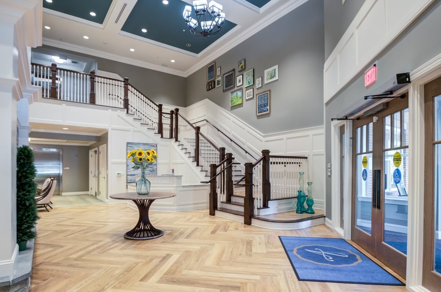 The grand, light-filled entryway at Arbor Terrace Morris Plains features elegant hardwood floors, a sweeping staircase, and fresh floral accents, welcoming residents and families to this exceptional assisted living community in Morris Plains, NJ.