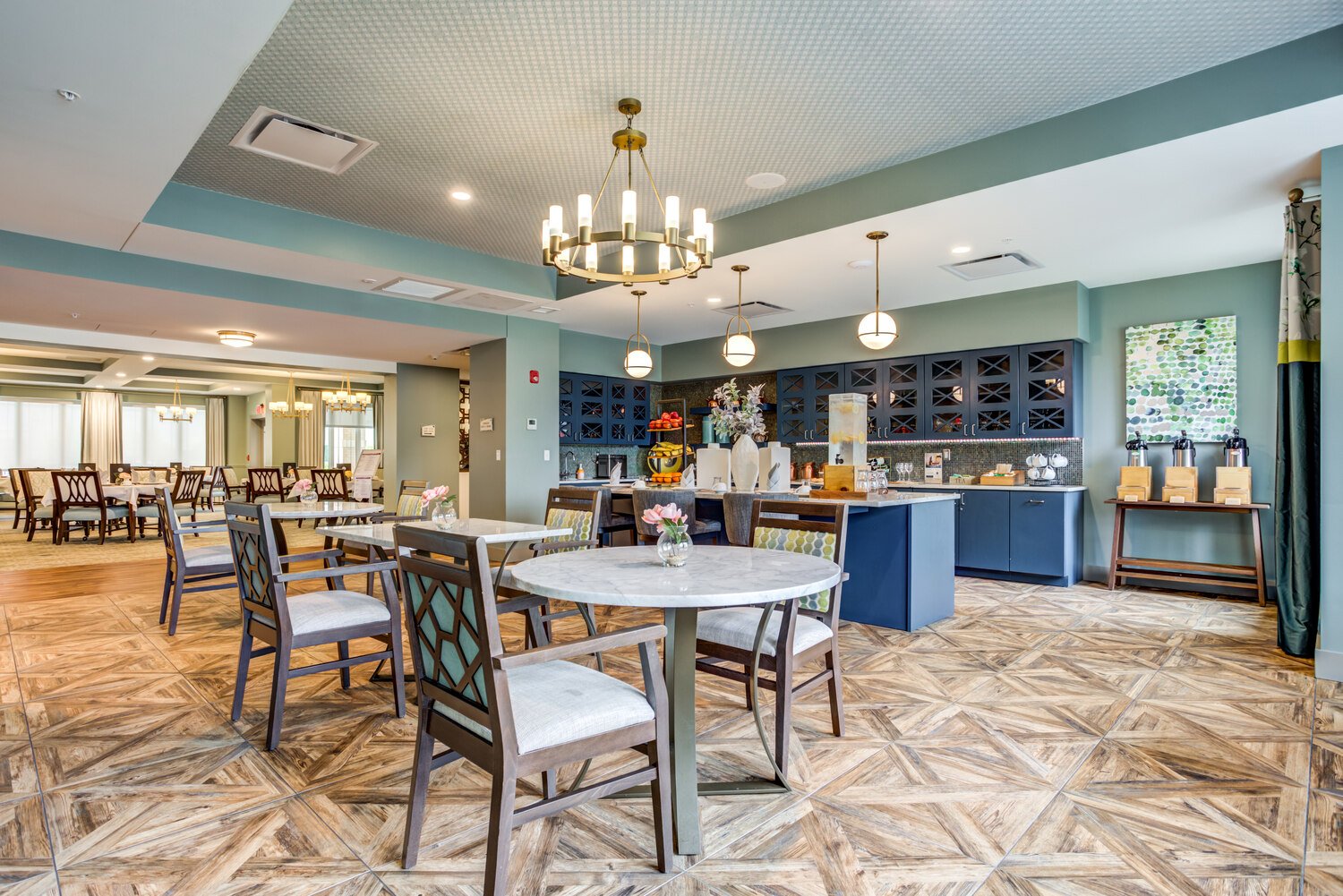Arbor Terrace Naperville Dining area with a patterned wooden floor. Two top tables and a blue bar and shelves in the background. Chandelier on the ceiling 
