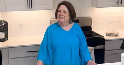 A woman in blue smiling in her kitchen