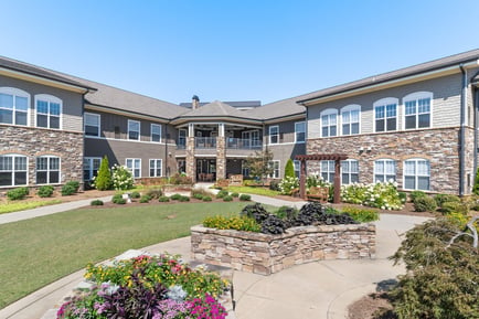 The beautifully landscaped courtyard and stone exterior of Arbor Terrace South Forsyth, named best senior living community in Suwanee, GA by U.S. News and World Report.