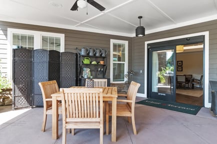 A charming covered outdoor patio with a wooden table and chairs, garden décor, and an open entry at Arbor Terrace, a welcoming senior living community in Suwanee, GA