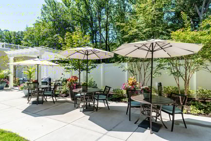 A beautifully landscaped outdoor patio with shaded seating, colorful flowers, and lush greenery, perfect for enjoying the fresh air at our senior living community in Gambrills, MD.