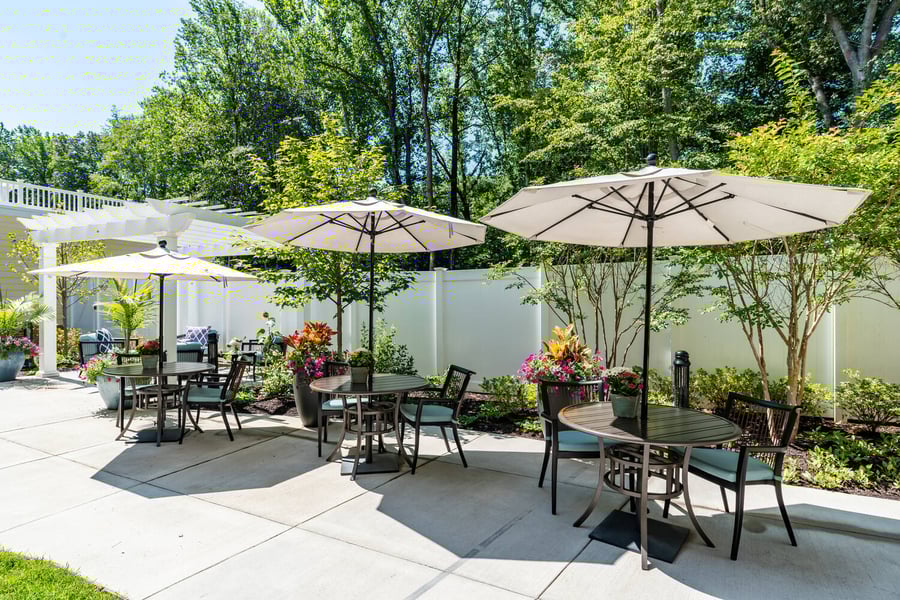 A beautifully landscaped outdoor patio with shaded seating, colorful flowers, and lush greenery, perfect for enjoying the fresh air at our senior living community in Gambrills, MD.