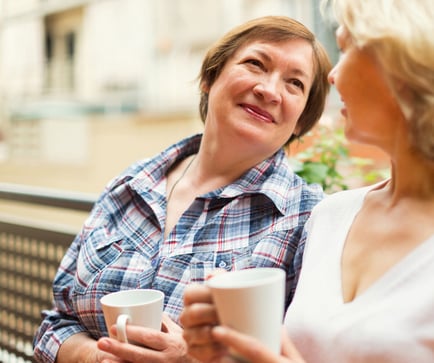 A woman smiles warmly while sharing a conversation over coffee with a companion, capturing the welcoming connections available at a senior living community in Burlington County.