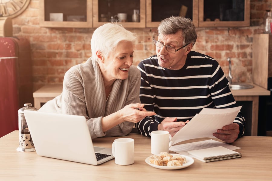 a senior couple discussing paperwork while using a laptop and having coffee