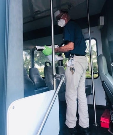 A staff member wearing green gloves carefully sanitizes the interior of a community transport vehicle at assisted living in Fort Myers, FL, ensuring a clean and safe environment for residents.