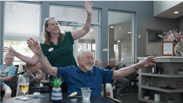 A staff member and residents enthusiastically joining in a group activity at Arbor Terrace Lakeway, showcasing the joyful and engaging lifestyle of this assisted living Lakeway TX community.
