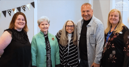 Residents, staff, and guests smile with arms around each other at a special event at Arbor Terrace Highland Park. Gatherings like this reflect the active senior lifestyle and senior living in Highland Park, IL.