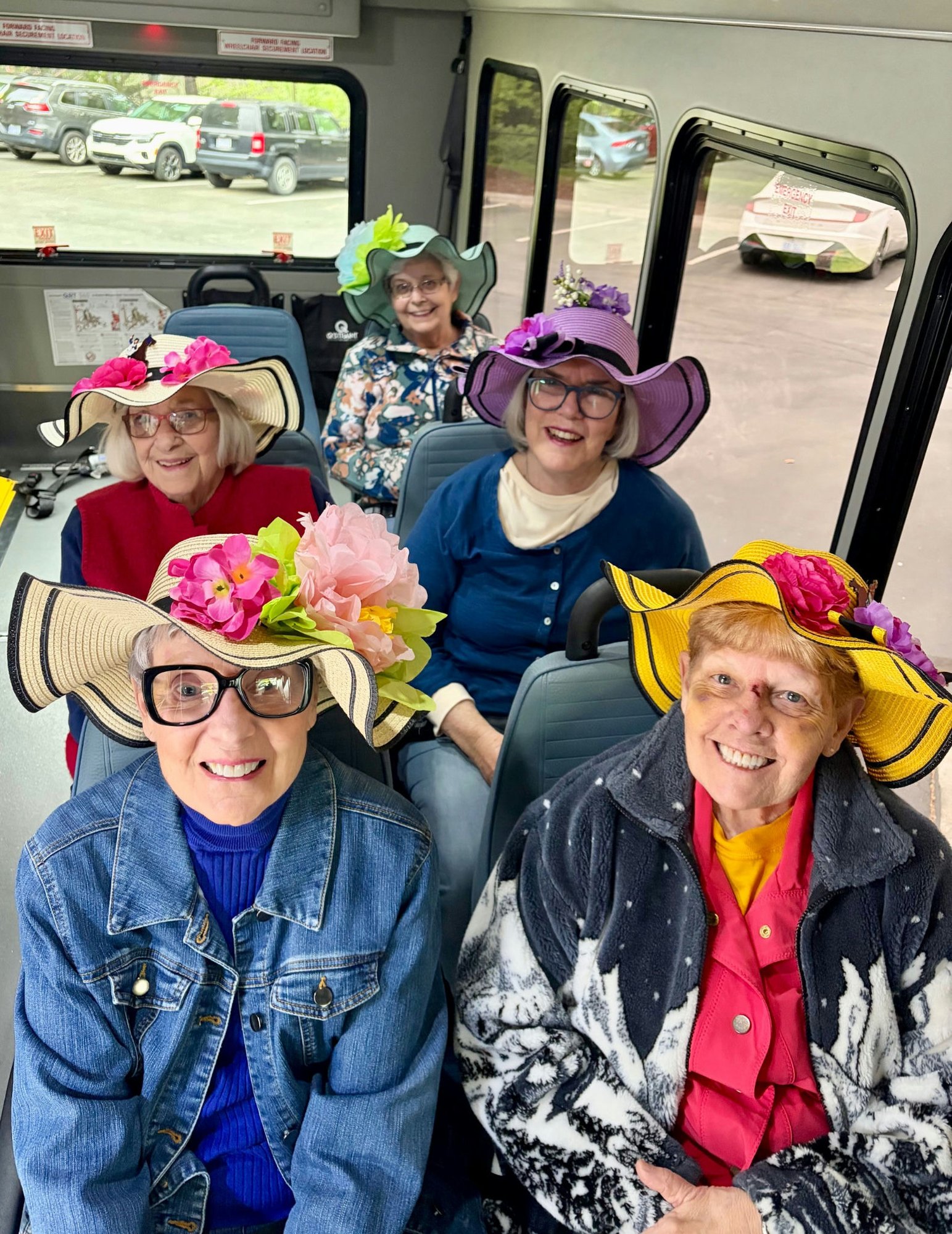 A group of residents wearing colorful sun hats ride together on a shuttle, enjoying a playful outing and community connection at The Arbor Company.