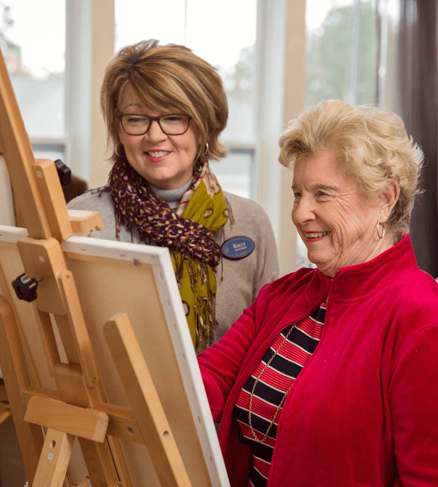 Staff member with resident at easel, painting