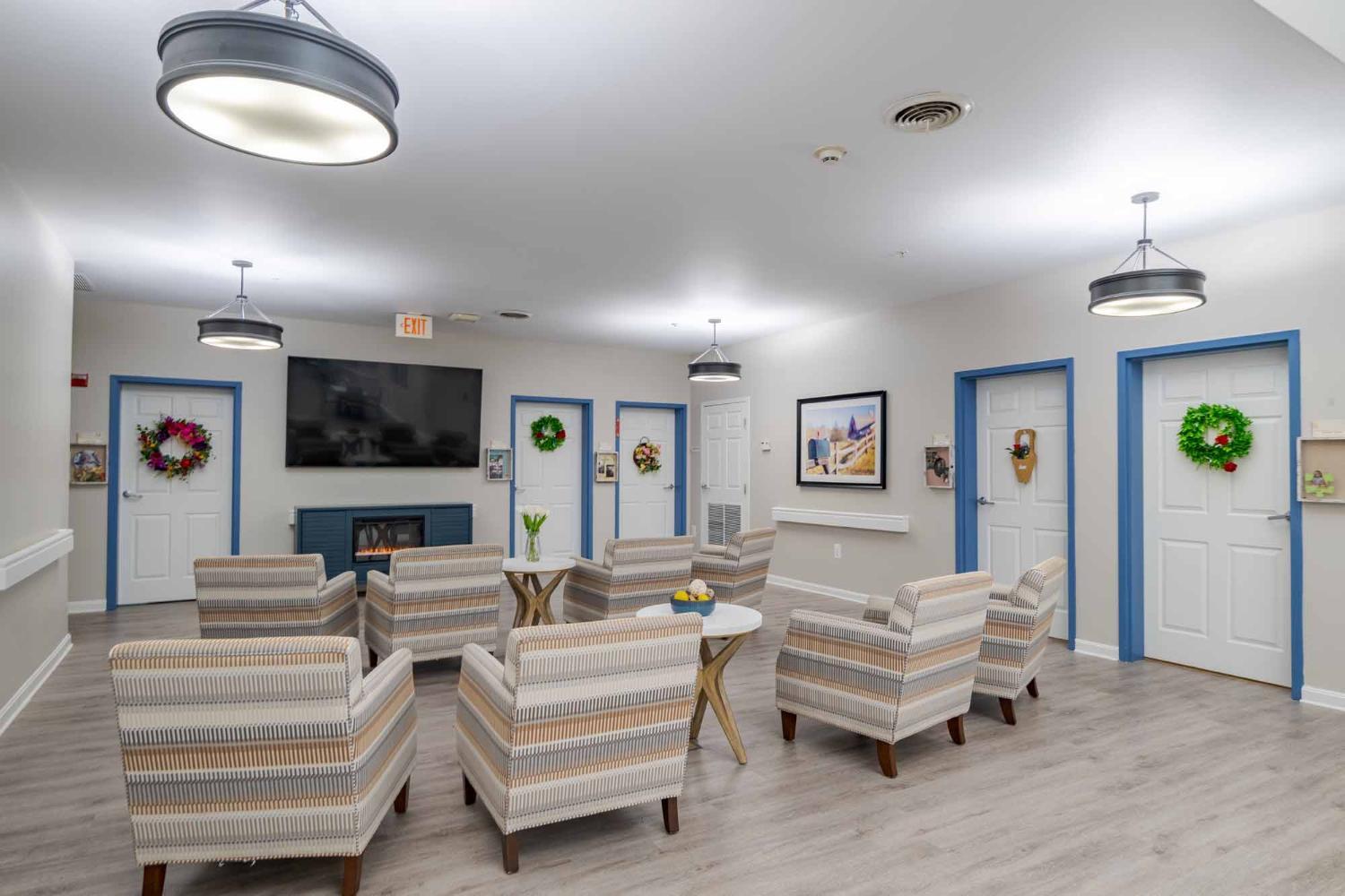 Entertainment area with a mounted television at the middle with a fireplace underneath. Arm chairs and coffee tables around. 